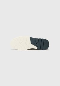 Sole of a sneaker featuring a textured design with a white rubber base and a dark blue accent. The tread has zigzag patterns for traction.