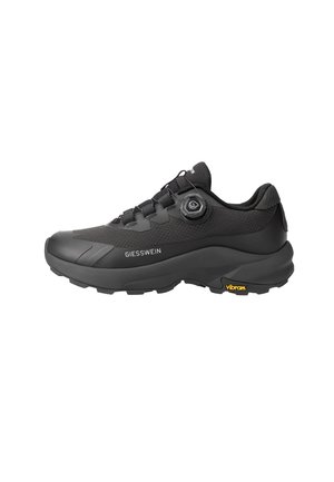 Schwarzer Giesswein Sneaker mit strukturiertem Obermaterial, Schnürverschluss mit Drehverschluss, dicker Sohle und Vibram-Logo an der Fersensohle, seitliche Ansicht.