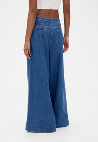 Blå denimbyxor med vida ben och hög midja, med bakfickor och slät textur. Nedre kanten är lätt utsvängd.