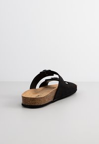 Sandale à brides en suède noir avec design découpé, semelle en liège et semelle extérieure en caoutchouc texturé, équipée d'une sangle ajustable pour un bon maintien.