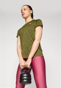 Grønn melert treningst-skjorte med korte ermer, kombinert med blanke rosa tights; holder en svart kettlebell med teksturert grep.