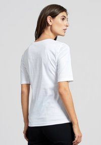 T-shirt bianco a maniche corte con scollatura rotonda, tessuto morbido e vestibilità classica. La vista posteriore mostra un design senza cuciture e uno stile semplice.