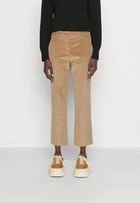 Pantalones de pana beige con corte recto y sutiles costillas verticales, combinados con zapatillas marrones y una camiseta negra de manga larga.