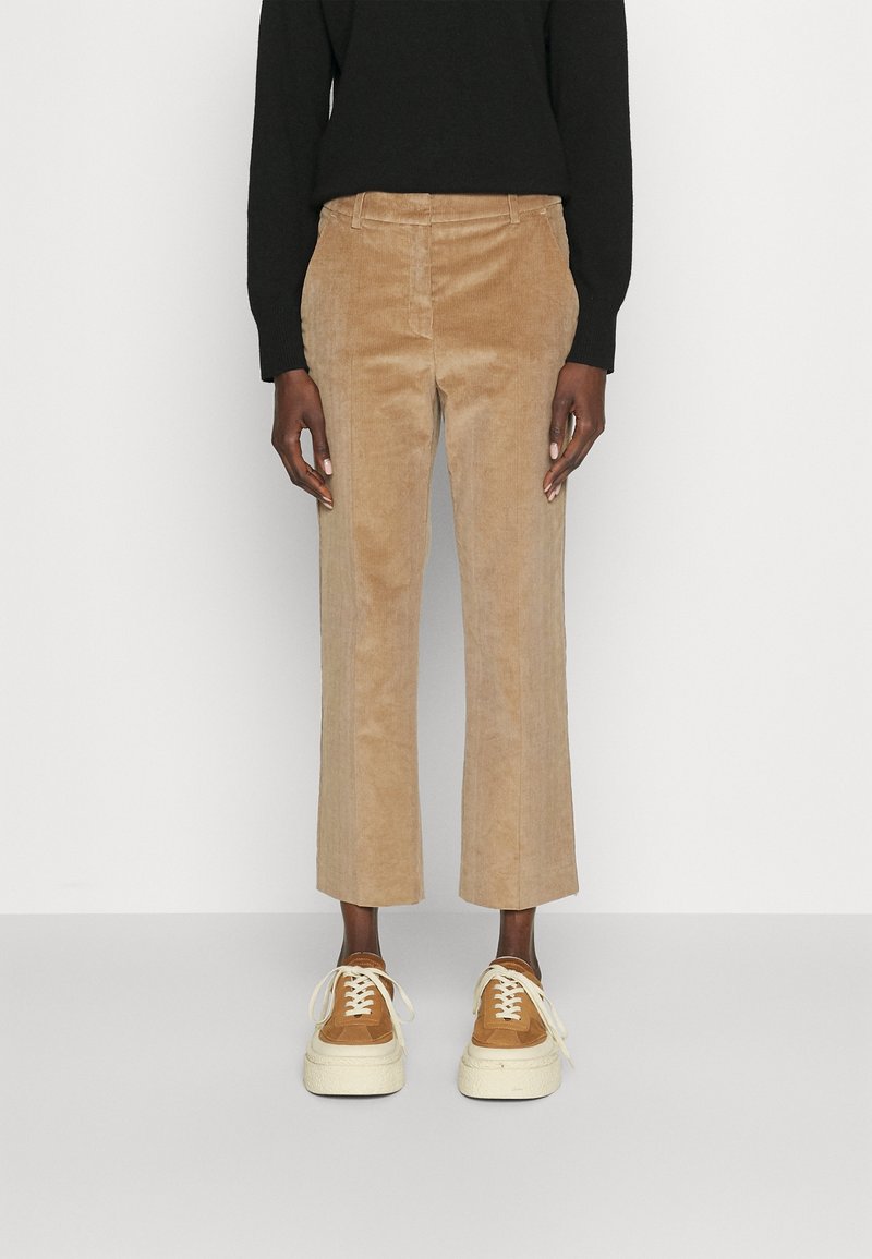 Pantalones de pana beige con corte recto y sutiles costillas verticales, combinados con zapatillas marrones y una camiseta negra de manga larga.