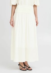 Jupe maxi blanche avec une taille smockée, en tissu fluide et d'une texture légère. Associée à des sandales à lanières noires.