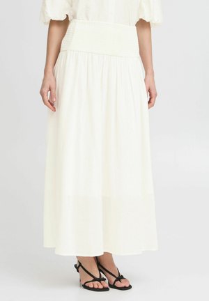 Witte maxi rok met een smockband, vloeiende stof en een lichte textuur. Gecombineerd met zwarte sandalen met bandjes.