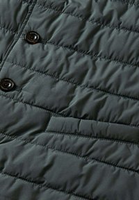 Gesteppte dunkelgrüne Jacke mit glatter Textur, ausgestattet mit schwarzen Knöpfen und einer Seitentasche. Kompaktes, leichtes Design für Wärme.