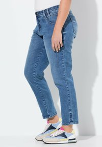 Jean en denim bleu clair avec une coupe droite, dotée d'une fermeture à bouton et de poches latérales, associée à des baskets de sport multicolores.