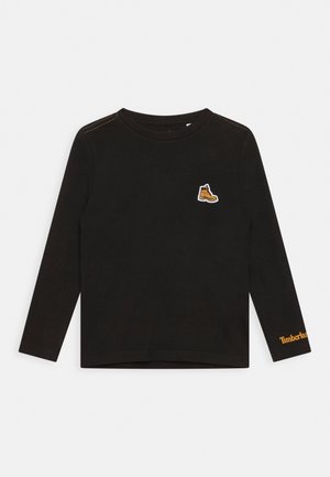 Czarna koszula z długim rękawem z okrągłym dekoltem, małą żółtą naszywką w kształcie buta na klatce piersiowej oraz napisem "Timberland" w kolorze żółtym na mankiecie lewego rękawa.