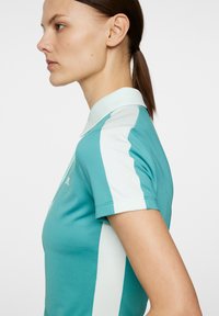 Teal polo skjorta med en texturerad tyg, som har en ljusblå krage och sidokanter. Korta ärmar; slim fit-design.