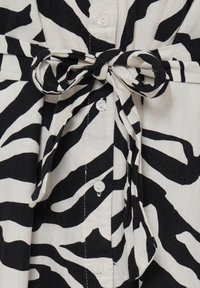 Tissu zébré noir et blanc noué en nœud papillon sur des boutons blancs sur la fermeture avant d'un vêtement.