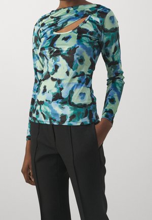 Haut ajusté à manches longues avec motif abstrait bleu, vert et noir, détail découpé près de la clavicule, assorti à un pantalon noir taille haute.