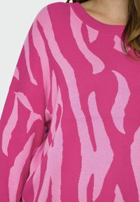 Pulover fucsia cu un model abstract în valuri de culoare roz deschis, având un guler rotund cu ramă și mâneci lejere, realizat dintr-un material tricotat moale.