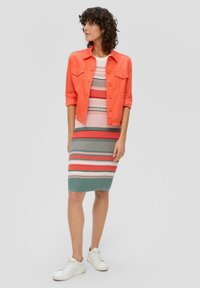 Veste en denim corail sur une robe en tricot rayée rose, verte et rouge, associée à des baskets blanches. La robe présente un design ajusté et une texture côtelée.
