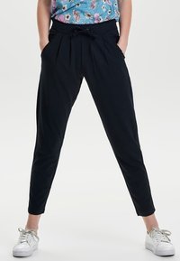 Pantaloni jogger navy con vita elasticizzata, tasche anteriori e cordino. Gambe affusolate e tessuto leggero. Abbinate a sneakers bianche.