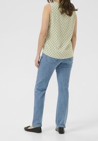 Ljusgrön ärmlös topp med svarta prickar, i kombination med blå raka jeans och svarta lägenheter, sedd från baksidan.