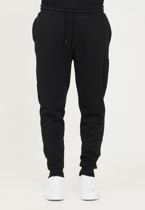 Pantalons de survêtement noirs avec une taille élastique et des chevilles resserrées. Fabriqués en matériau doux, avec une poche de chaque côté. Baskets blanches.