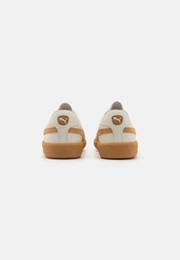 White leather sneakers with brown rubber soles, featuring textured accents, a padded collar, and a small logo on the back near heel.