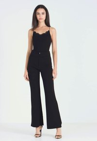 Svart ermeles bodysuit med blonder trim, kombinert med høyt liv, vide svarte bukser og sandaletter med stropper. Glatt stofftekstur.