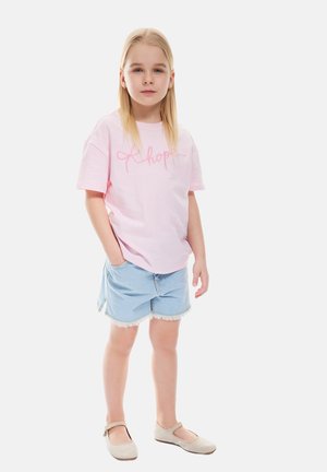 Lyserød bomulds T-shirt med broderet tekst, parret med lyseblå denimshorts med frynser, og beige flade sko.
