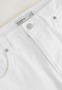 Hvide denimjeans med sølvknaplukning, bæltestropper og en størrelseslabel, der viser 34R fra N. Premium Collection.