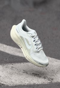 Ανοιχτό γκρι παπούτσι για τρέξιμο με πλέγμα στο πάνω μέρος, υφασμένο σχέδιο και λευκές λεπτομέρειες. Διαθέτει μαξιλαρωμένη σόλα και παραδοσιακό σύστημα δέσιμου με κορδόνια.