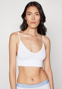 Valkoinen ribbineulottu bralette, jossa ohuet hihnat ja syvä V-mallinen pääntie, yhdistettynä valkoisiin alaosiin, joissa on vaaleansininen joustava vyötärönauha, jossa lukee "PIECES".