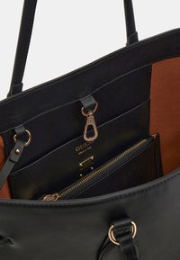 Zwarte leren schoudertas met een gladde textuur, voorzien van gouden hardware, binnenzakken en een bruine voering. Verschijnt met een geäväde compartiment.