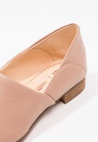 Chaussure en cuir rose clair avec un bout rond et un petit talon en bois. Texture lisse avec un design simple et sans embellissements visibles.