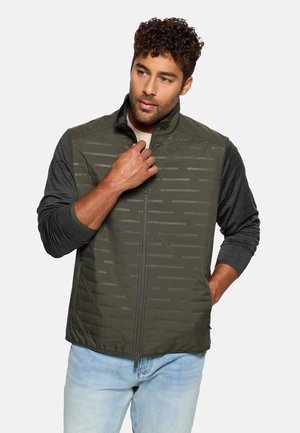 Chaleco verde oliva con cremallera y un frente texturizado, capa base de manga larga gris debajo y un ajuste relajado. Cuenta con un patrón sutil.