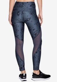 Leggings grigio scuro con un motivo astratto nero, dotati di inserti in rete e una fascia in vita ampia. Abbinati a scarpe da ginnastica nere.