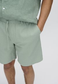 Light green shorts made of textured fabric with an elastic waistband and drawstring, shown with a matching short-sleeve shirt.