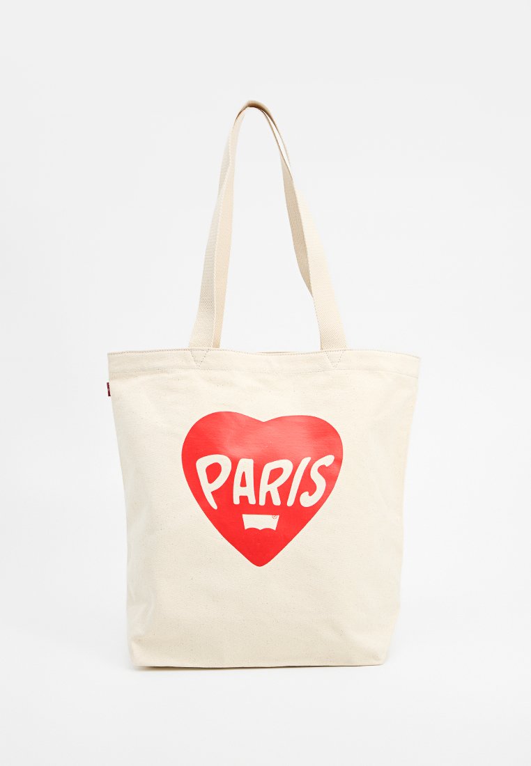 Sac fourre-tout en toile de couleur crème présentant un grand graphique d'un cœur rouge avec "PARIS" en texte blanc. Deux poignées en tissu robustes. Design simple.