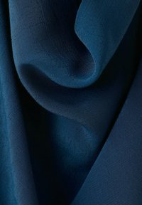 Temno modro blago z vidno tkanim vzorcem, mehko zloženim in ovitim, ki prikazuje kontraste svetlobe in sence.