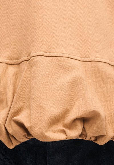 Μπεζ ύφασμα με ραμμένη ραφή και ελαστική άκρη που μαζεύει πάνω σε σκούρο μπλε τζιν υλικό.