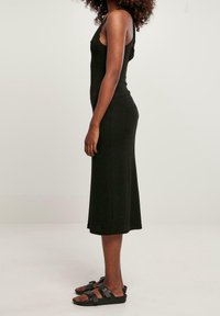 Černé žebrované midi šaty s tenkými ramínky, přiléhavým střihem a jemnou texturou. Kombinováno s černými plochými sandály se zapínáním na přezky.