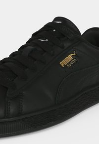 Μαύρο sneaker Puma Suede με υφή στην σόλα, μαύρα κορδόνια και χρυσό λογότυπο Puma στο πλάι.