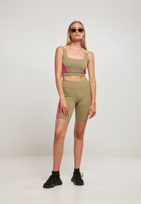 Oliven grønn sportsbh og shorts-sett med rosa og gule detaljer. Glatt, elastisk stoff; firkantet utringning; tettsittende design. Svarte joggesko.