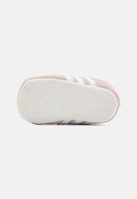 Zapatilla rosa con suela blanca y patrón de almohadilla en forma de chevron, mostrando la vista inferior sobre un fondo claro y liso.