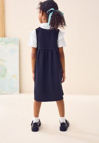 Czarna sukienka bez rękawów z marszczeniem z tyłu, noszona na białej koszuli z kołnierzykiem. Czarne buty i białe skarpetki dopełniają strój. Niebieska wstążka w kratkę we włosach.