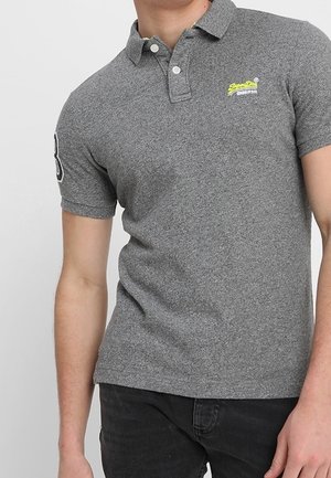 Szara koszulka polo z małym żółtym haftowanym logo, krótkimi rękawami i standardowym kołnierzykiem, wykonana z teksturowanej tkaniny.