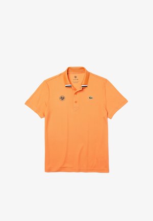 Pomarańczowa polo z krótkim rękawem z prążkowanym kołnierzykiem w czarno-białe paski, trzy guzikowy dekolt, oraz małe logo na piersi.