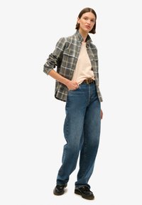 Chemise en flanelle à carreaux gris et bleu sur un t-shirt rose pâle, associée à un jean bleu taille haute et des chaussures noires à lacets.