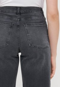 Jeans alti in vita di colore grigio scuro, realizzati in denim, con due tasche posteriori, una struttura liscia e un design aderente.