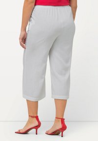 Grijze cropped broek met een gestructureerde afwerking en eenGathered tailleband, gecombineerd met rode enkelband hakken. De broek heeft opgerolde mouwen.