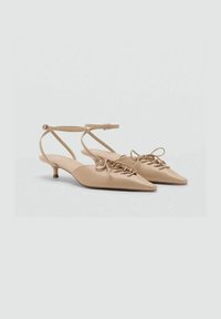 Des chaussures slingback beige à bout pointu avec un petit talon, présentant une surface texturée et un laçage sur le devant.