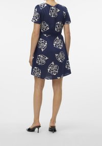 Marinblå klänning med vitt blommönster, korta ärmar och lös passform, tillsammans med svarta öppna klackskor. Slät tygtextur.