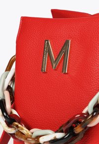 Červená kožená kabelka s texturem, která se může pochlubit velkým zlatým logem "M" a vícebarevným řetízkem s různými lesklými články.