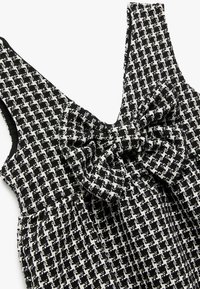 Schwarzes und weißes Tweed-Kleid mit V-Ausschnitt, Schleifenakzent am Ausschnitt und einem strukturierten, gemusterten Stoff mit formgebender Schnittführung.