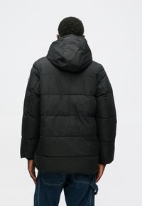 Mustat toppatakki hupulla, jossa on tikattu kuvio ja nopeudella teksturoitu kangas. Sormipäällysteet ja rento istuvuus.